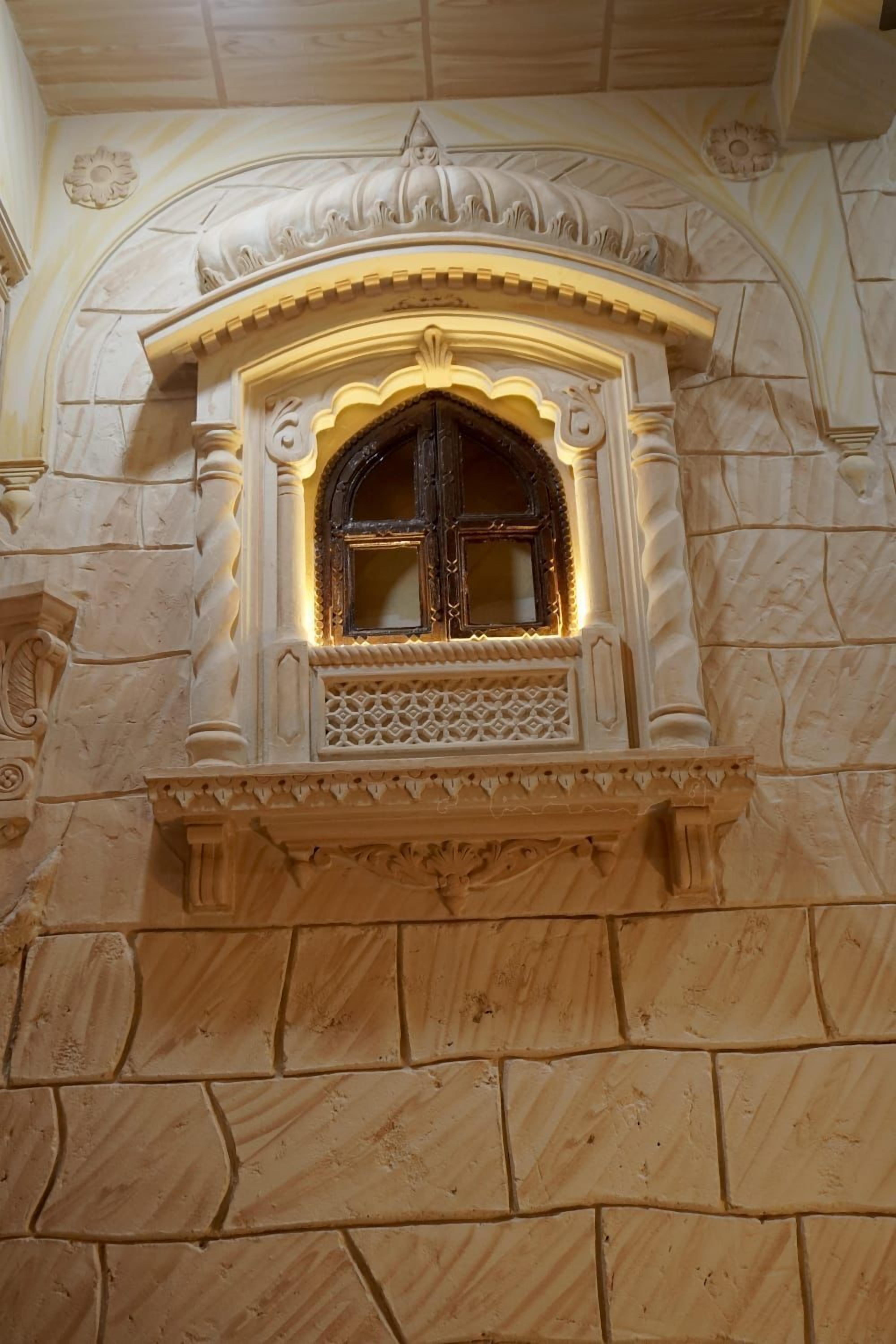 A stone wall with a decorative window featuring intricate carvings and a small balcony.