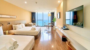 Habitación de hotel con dos camas, televisión, escritorio y vista al mar.