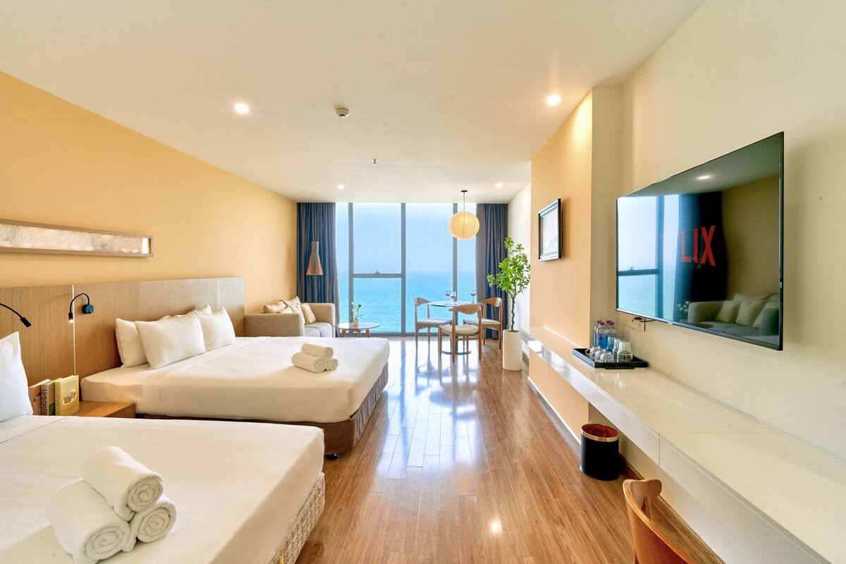 Habitación de hotel con dos camas, televisión, escritorio y vista al mar.