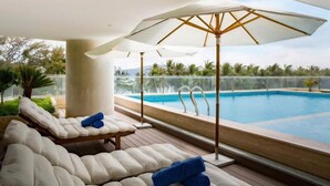 Zona junto a la piscina con dos sillones reclinables, una sombrilla grande y una vista despejada de la piscina y la vegetación circundante.