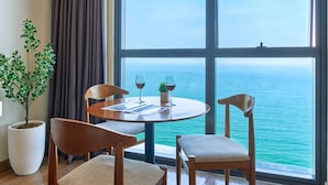 Un comedor con una mesa redonda, cuatro sillas de madera, una planta en maceta y vistas al mar a través de amplios ventanales.