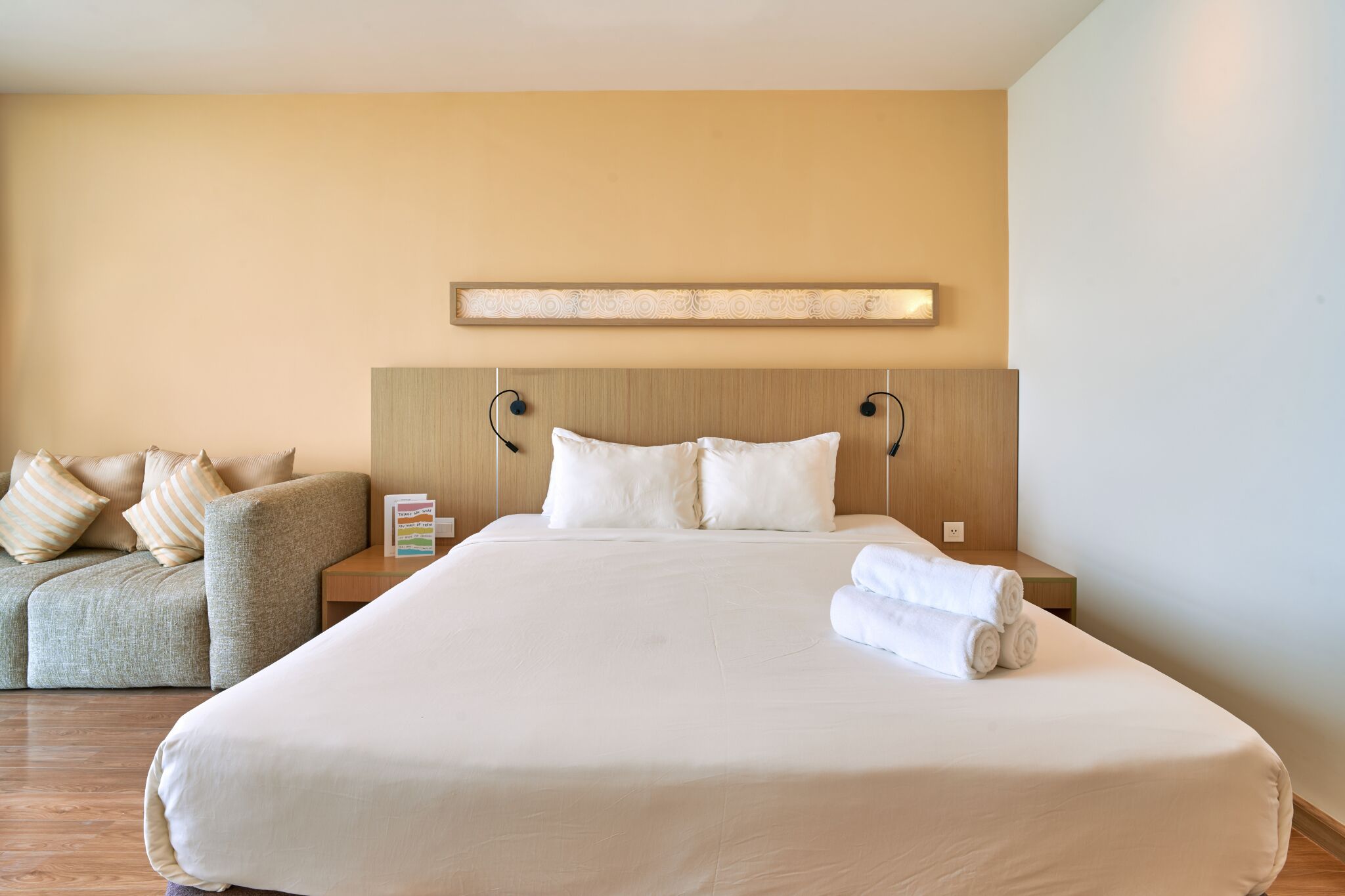 A hotel room with a large bed, a sofa, and a nightstand with a lamp.