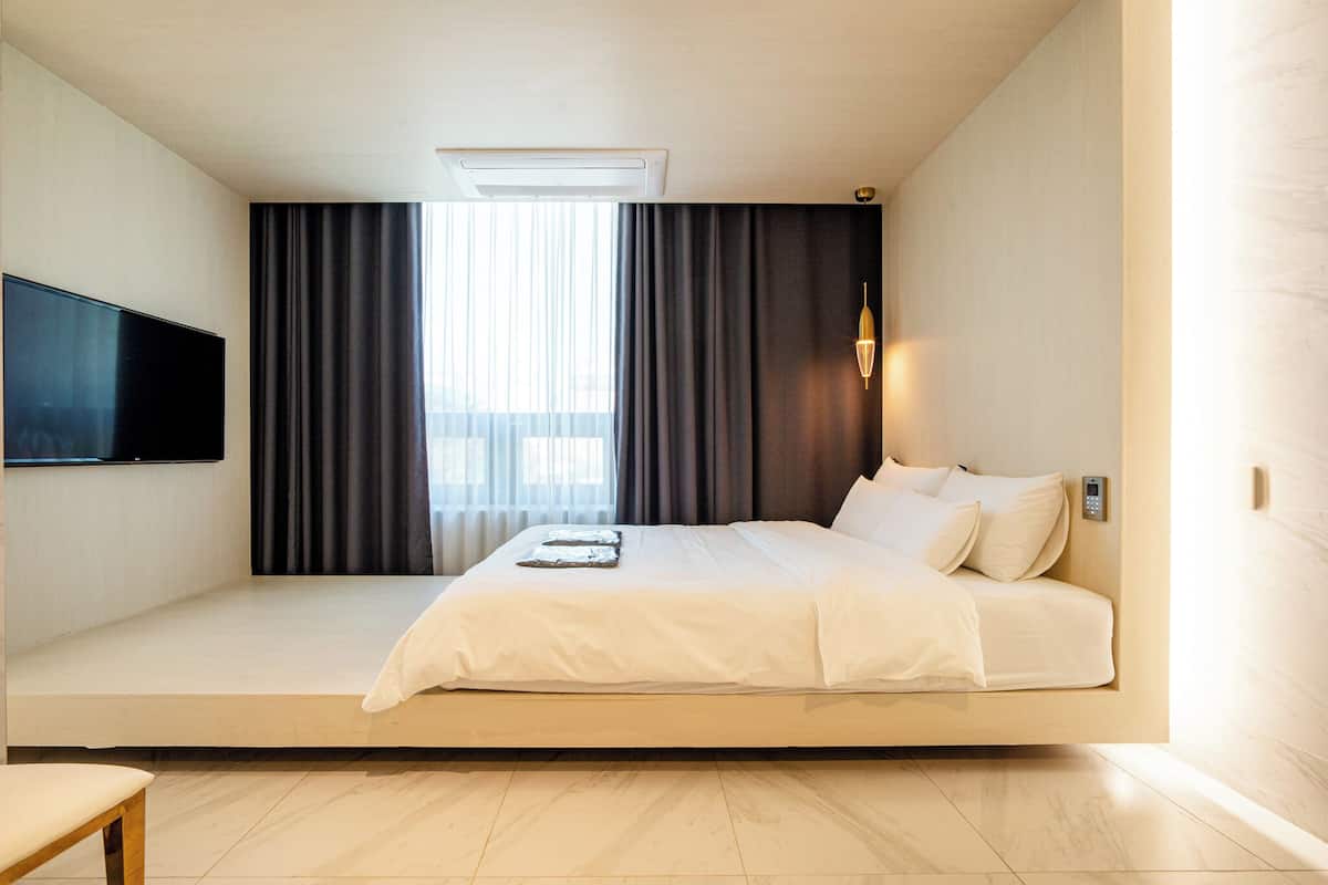A modern hotel room with a large bed, a flat-screen TV, a bedside table, and a window with curtains.