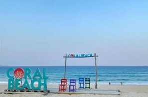 A beach sign with 'CORAL BEACH' written on it, and colorful chairs in front. - Haki Seaview (Bac Cam Ranh)