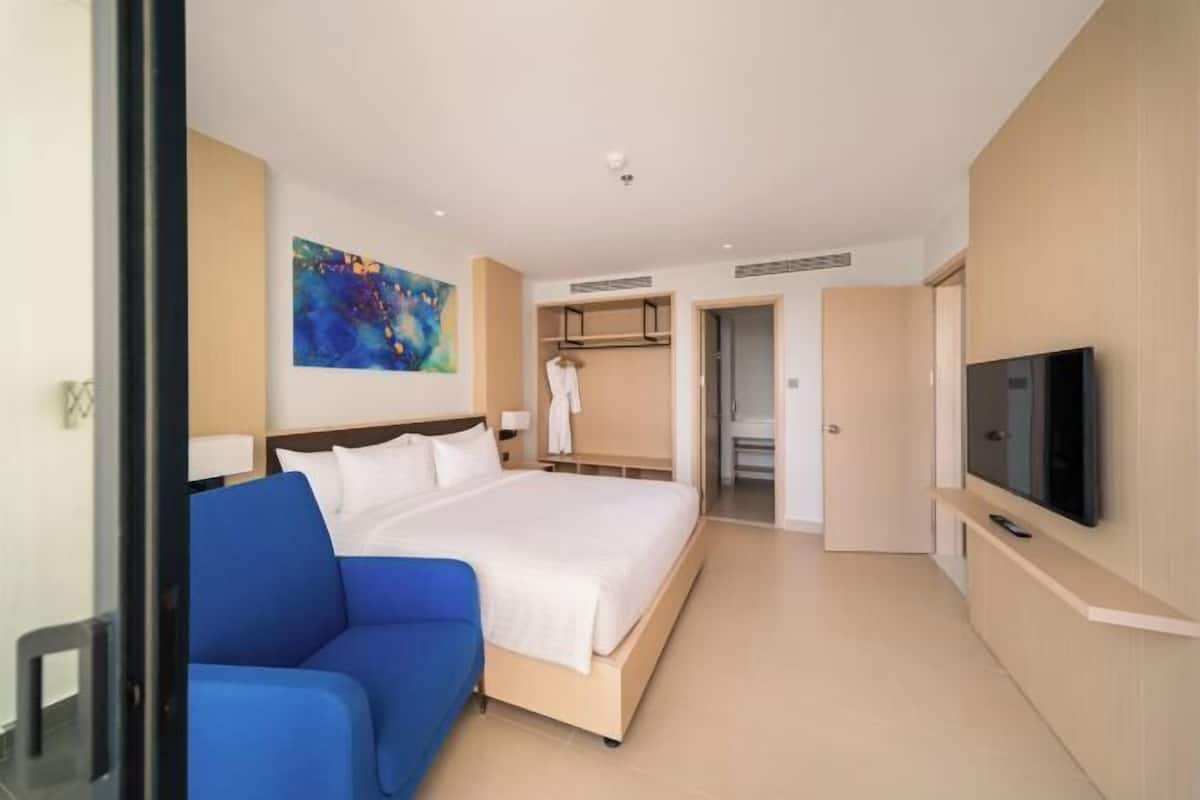 A hotel room with a large bed, a blue sofa, a TV, and a wardrobe.