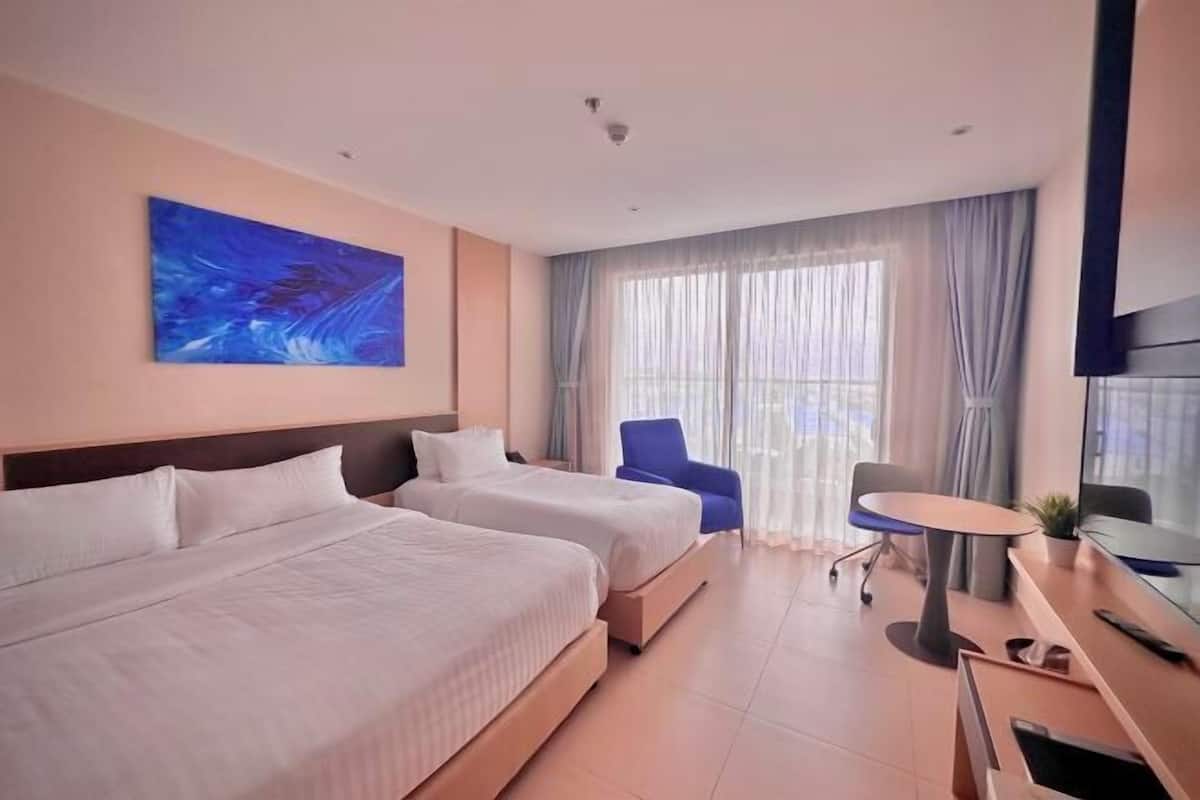 A hotel room with two beds, a desk, a chair, and a large window with curtains.