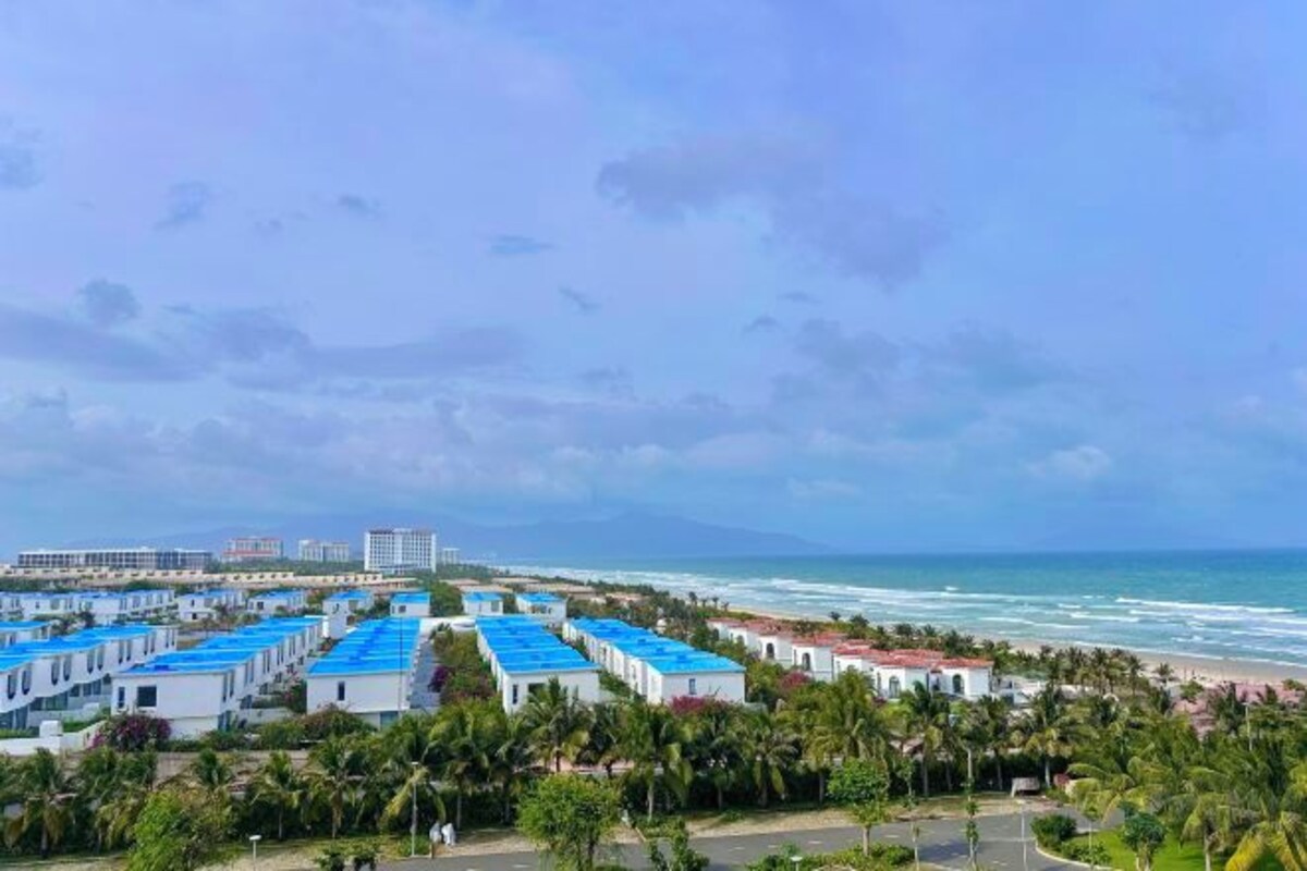 A coastal hotel with multiple blue-roofed buildings, a beach, and palm trees.