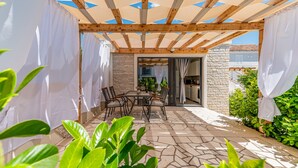 Une terrasse extérieure dotée d’une pergola en bois, d’un sol en pierre et d’une table avec des chaises.