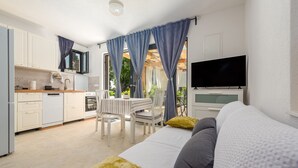 Une cuisine moderne avec des meubles blancs, un coin repas comprenant une table et des chaises, et un téléviseur fixé au mur.