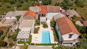 Une vue aérienne d’un quartier résidentiel avec une piscine centrale, entourée de maisons aux toits recouverts de tuiles rouges et présentant un mélange de styles architecturaux.