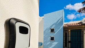 A white wall with a black intercom, a blue wall with two windows, and a tiled roof.