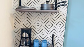 A compact kitchen with a Hisense stove, a coffee maker, and blue mugs on shelves.