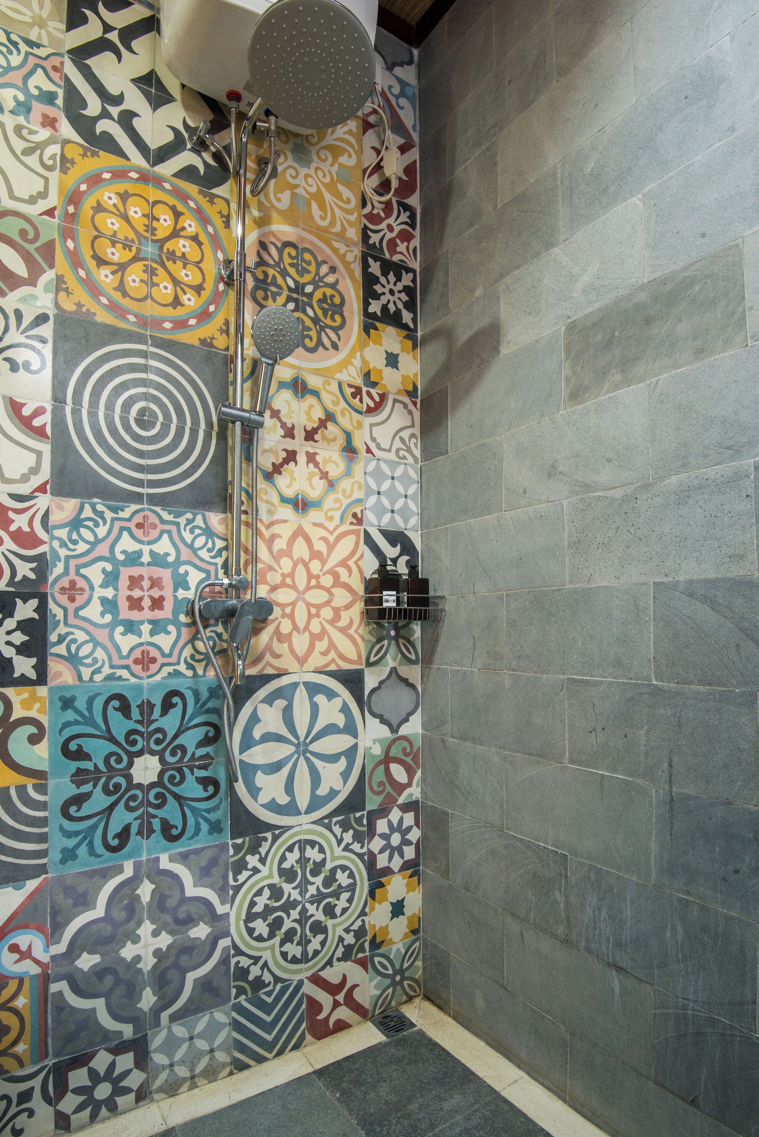 A shower with a colorful tile wall and a plain stone wall.