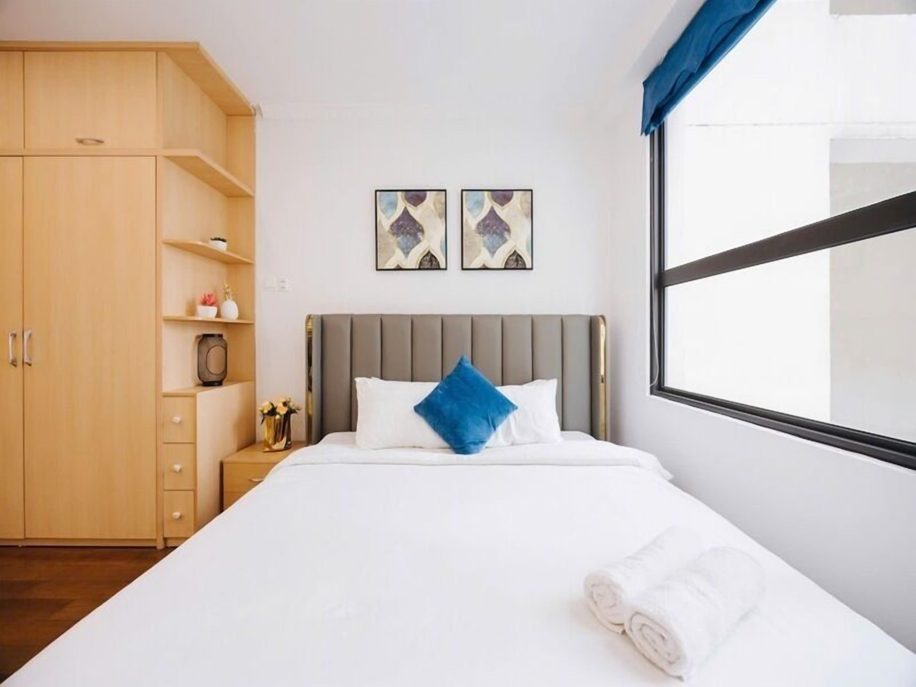 A hotel room with a bed, a wardrobe, a nightstand, and two wall-mounted artworks.