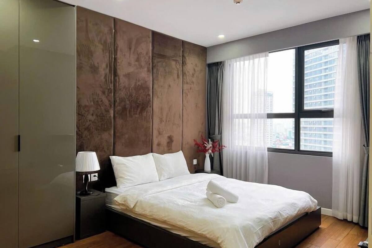 A modern bedroom with a large bed, a nightstand, a wardrobe, and a window with curtains.