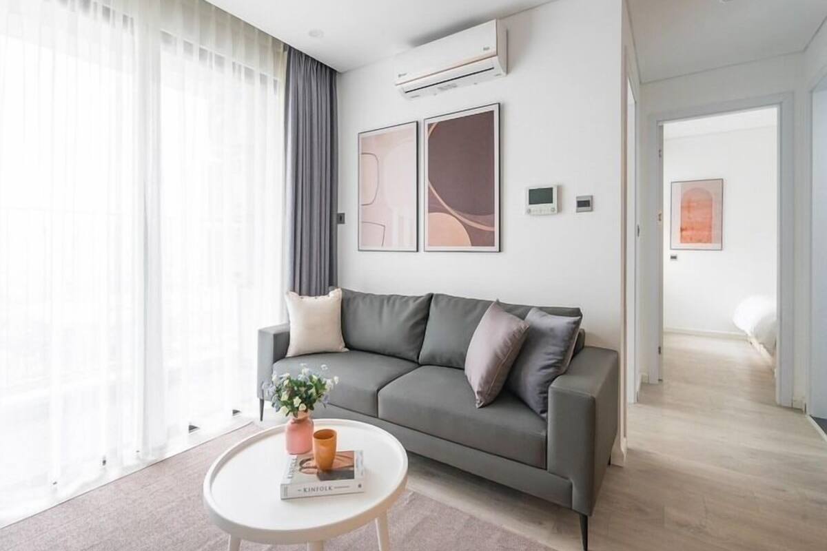 A modern living room with a grey sofa, a white coffee table, and a large window with sheer curtains.