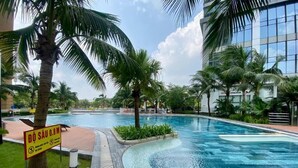 A swimming pool with palm trees, a sign indicating a depth of 0.8 meters, and a modern building in the background. - Vinhomes D'Capital - SunhouseLand (Hanoi)
