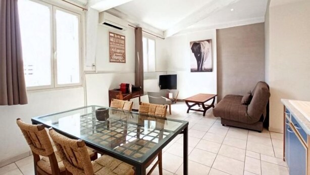 A living room with a glass-top table, chairs, a sofa, a TV, and a poster on the wall. - Central 1 Bedroom Place Marche Gambetta (Cannes)