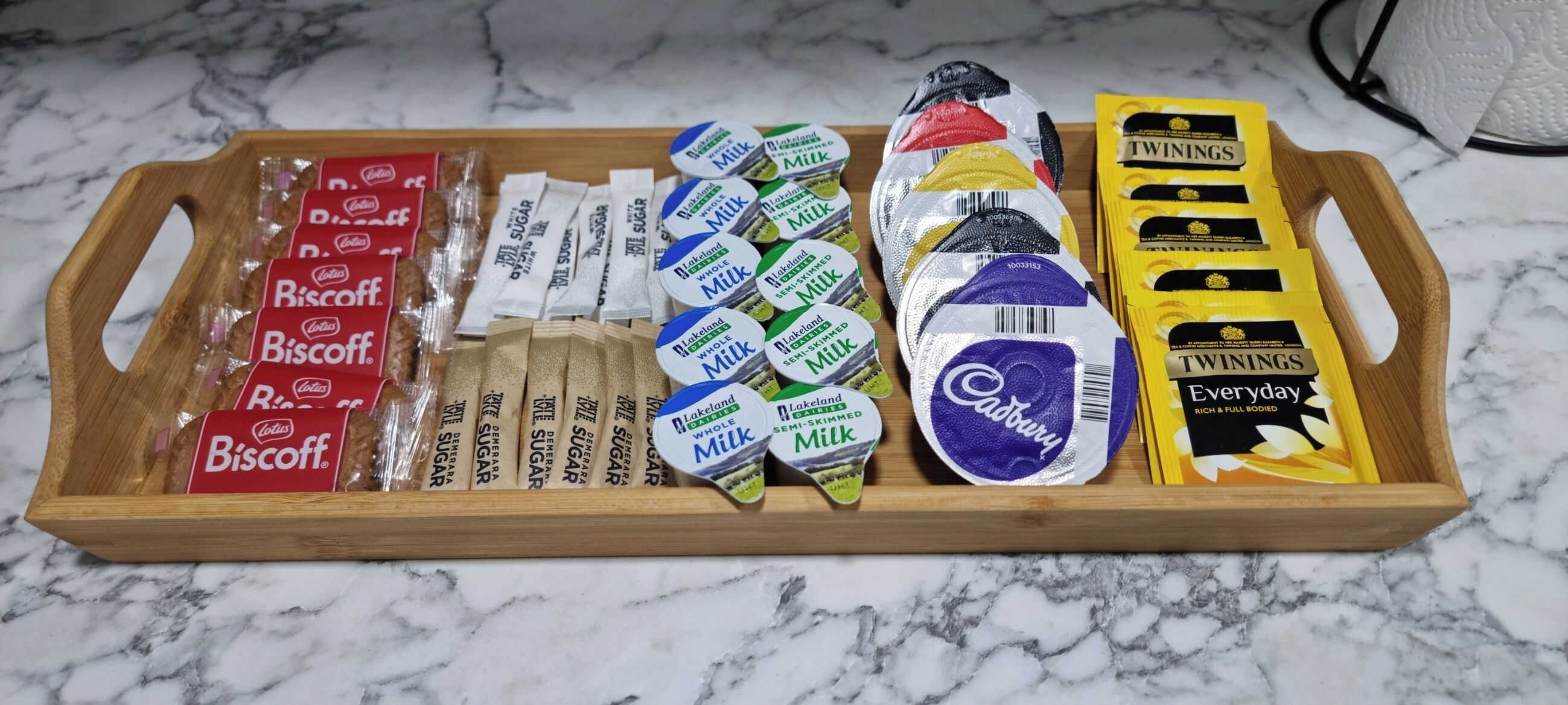 Una bandeja de madera con varios alimentos envasados, incluyendo galletas, leche y chocolates Cadbury.
