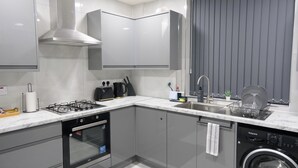 A modern kitchen with a gas stove, oven, dishwasher, and a compact washer-dryer unit. - Modern House - 3 Bedrooms - 1 Bath - ManCity (Manchester)