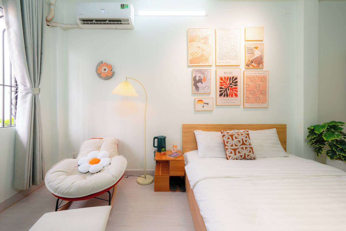A hotel room with a bed, a chair with a flower design, a nightstand with a lamp, and wall art.