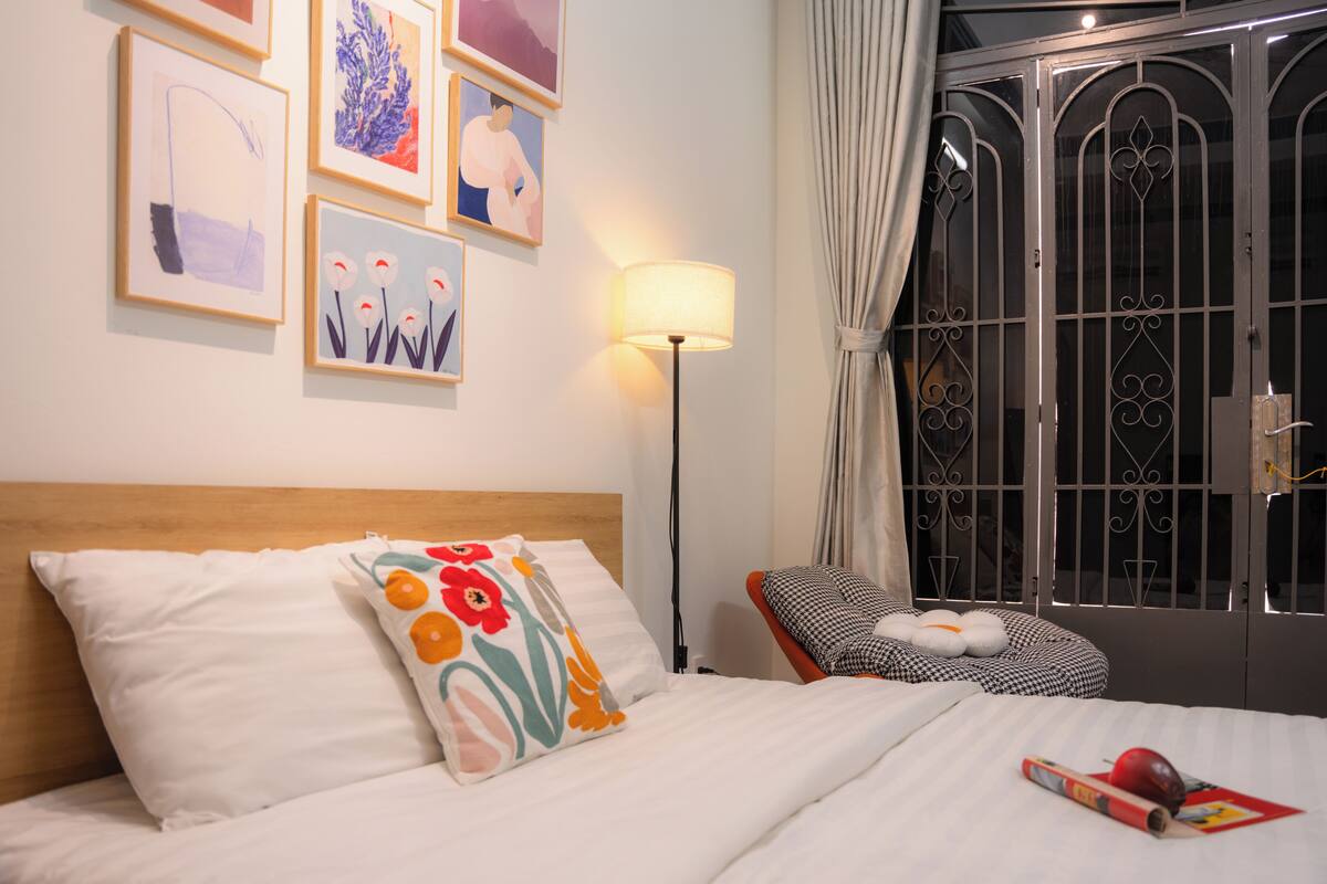 A hotel room with a bed, a lamp, a chair, and artwork on the wall.
