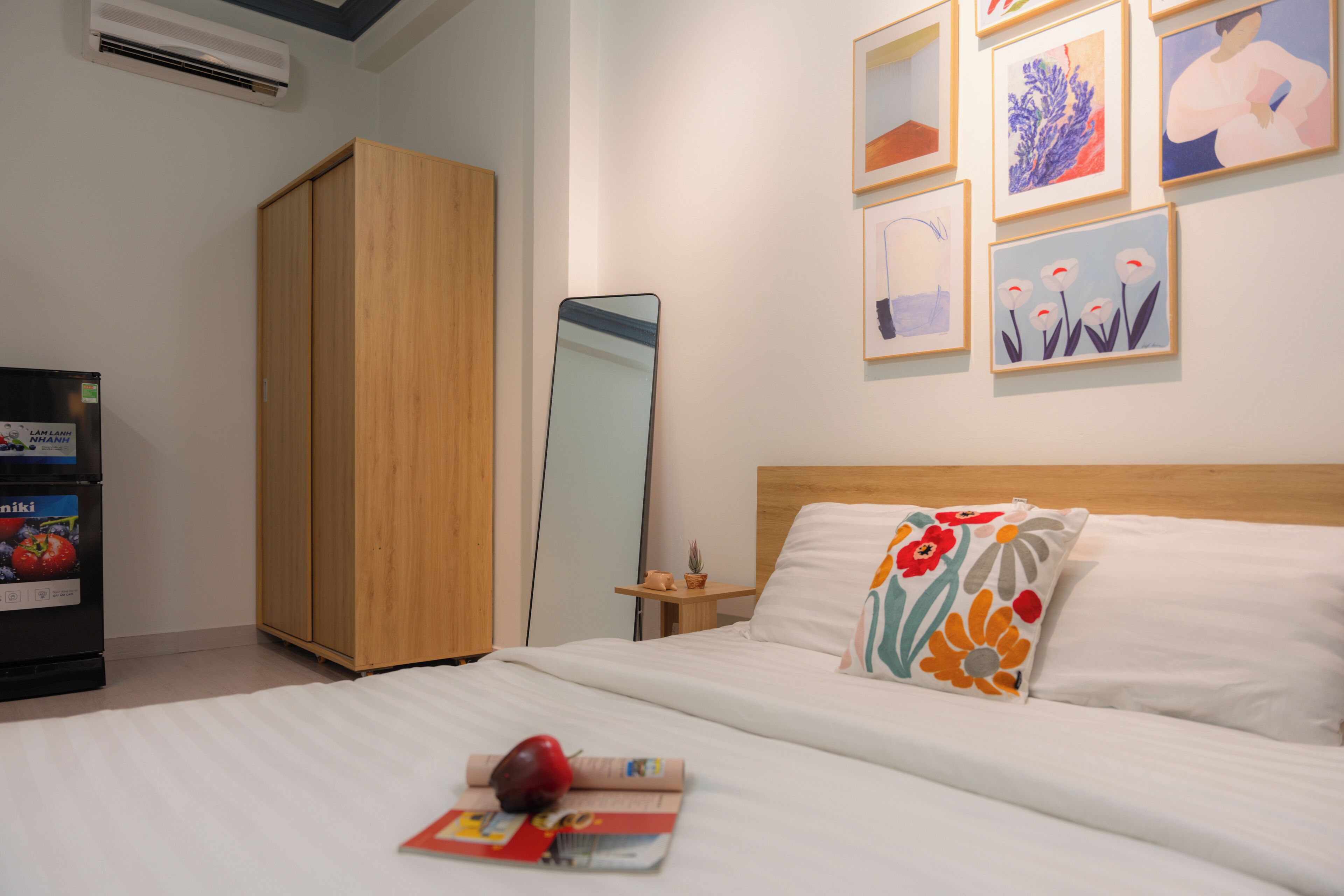 A hotel room with a bed, a wardrobe, a mirror, and artwork on the wall.
