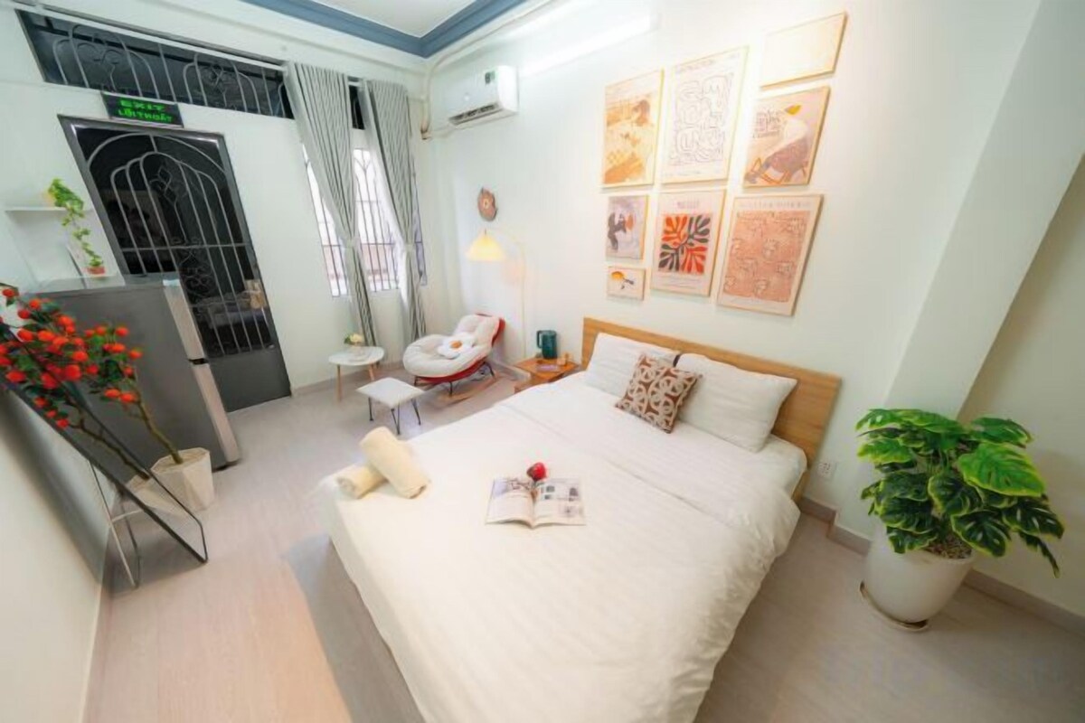 A hotel room with a bed, a desk, a chair, a potted plant, and artwork on the walls.