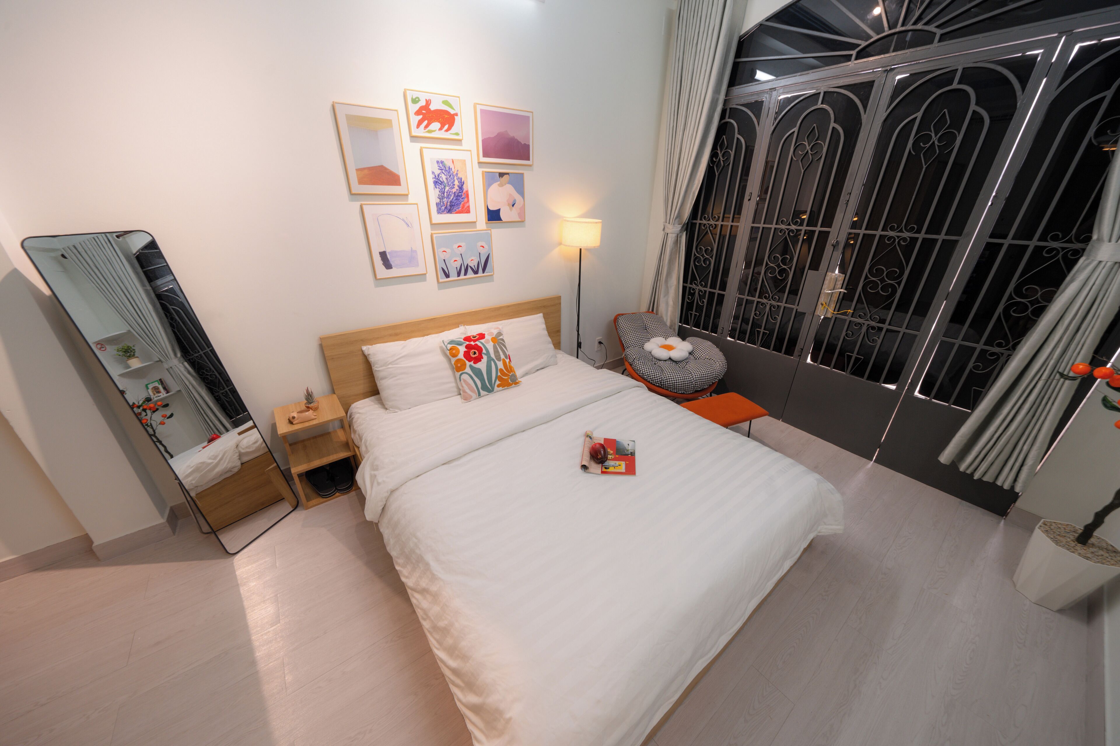 A neatly arranged bedroom with a bed, bedside table, lamp, and a large window with decorative metal grilles.