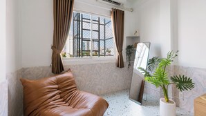 A room with a brown leather sofa, a large window with brown curtains, a potted plant, and a mirror on the wall. - Elysian Homestay (Ho Chi Minh City)