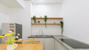 A compact kitchen with a wooden table, a built-in sink, and a black induction cooktop. - Elysian Homestay (Ho Chi Minh City)