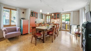 A spacious kitchen with wooden cabinets, a dining table, and chairs. There is a sofa and a television in the living area. - Casa Andy 2 Val Lavizzara with Views for Six, Piano di Peccia, Switzerland (Piano di Peccia)