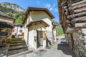 Una stretta via fiancheggiata da edifici in pietra tradizionali, con un ingresso ben visibile caratterizzato da una porta e delle scale, e una chiara vista di una montagna sullo sfondo.