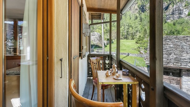 A wooden balcony with a table set for tea, overlooking a mountainous landscape. - Casa Andy 2 Val Lavizzara with Views for Six, Piano di Peccia, Switzerland (Piano di Peccia)