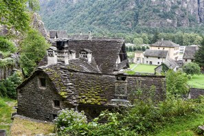 Un edificio de piedra con techo pronunciado, rodeado de vegetación exuberante y un paisaje montañoso.