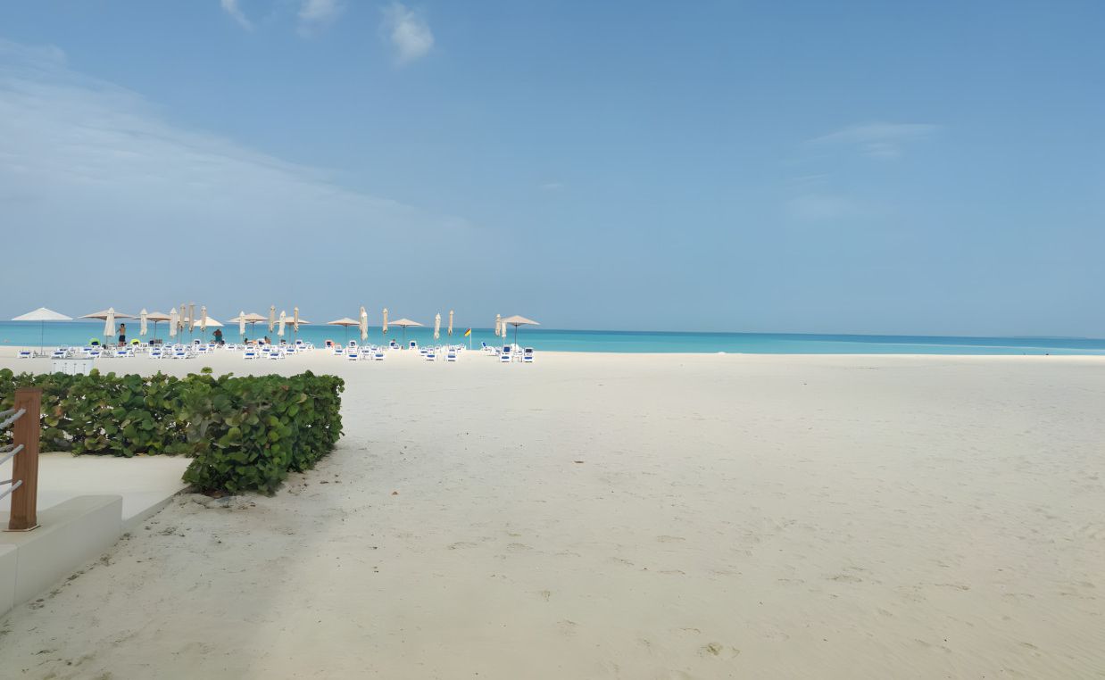 Una spiaggia con sabbia bianca, cielo azzurro limpido e ombrelloni.