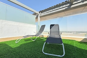 Two lounge chairs on a rooftop terrace with a clear view of the cityscape.