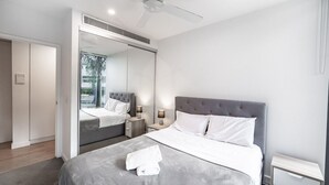 Une chambre à coucher moderne avec un grand lit, des tables de chevet, un ventilateur de plafond et un grand miroir.
