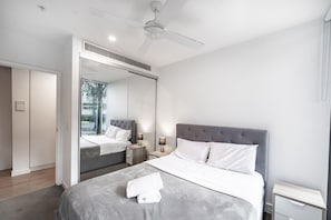 Een moderne slaapkamer met een groot bed, nachtkastjes, een plafondventilator en een grote spiegel.