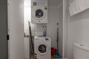 Kompakti pyykinhuoltotila, jossa on kaksi päällekkäin asetettua pesukonetta, pyykkiteline ja moppi.