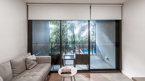 Un salon moderne avec un canapé, une petite table ronde et une porte-fenêtre coulissante donnant sur un balcon avec une piscine et de la verdure.