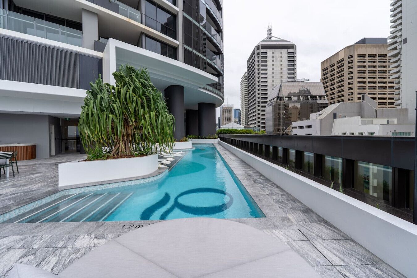 A rooftop pool with a modern design, surrounded by a high-rise building with balconies and a view of other buildings.