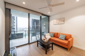 Un salon moderne doté d’une porte-fenêtre coulissante donnant sur un balcon, d’un ventilateur de plafond et d’un canapé agrémenté de coussins.