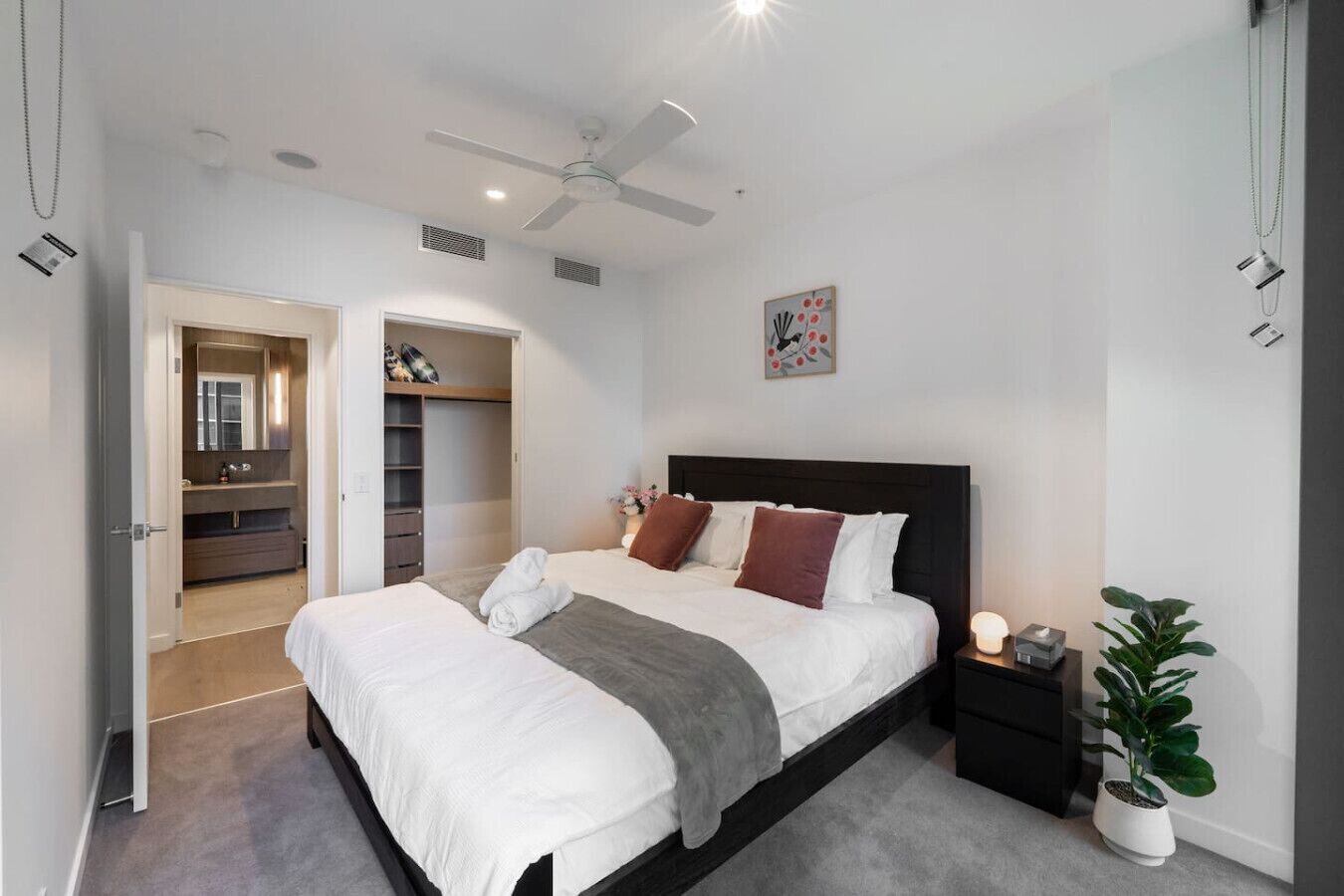 Une chambre moderne avec un grand lit, une table de chevet avec une lampe, un ventilateur de plafond et une plante en pot.