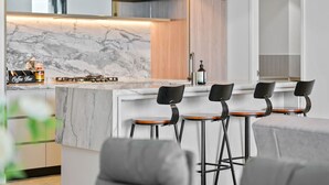 A modern kitchen with a marble countertop, black bar stools, and a coffee bar.