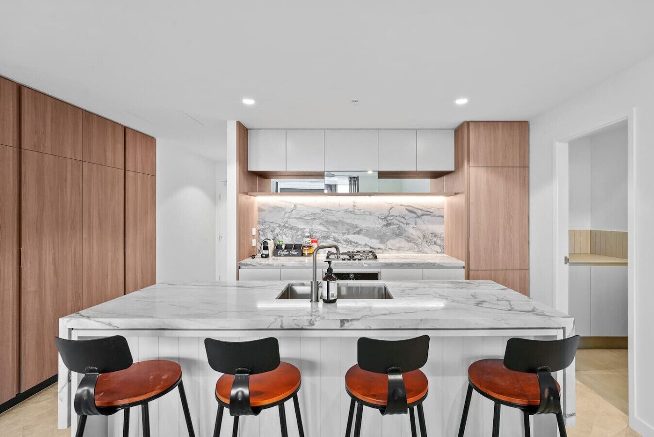 Una cocina moderna con encimera de mármol, una isla central con taburetes de bar y armarios de madera.