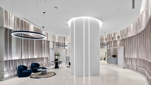 A modern lobby with a central column, seating area, and a reception desk.