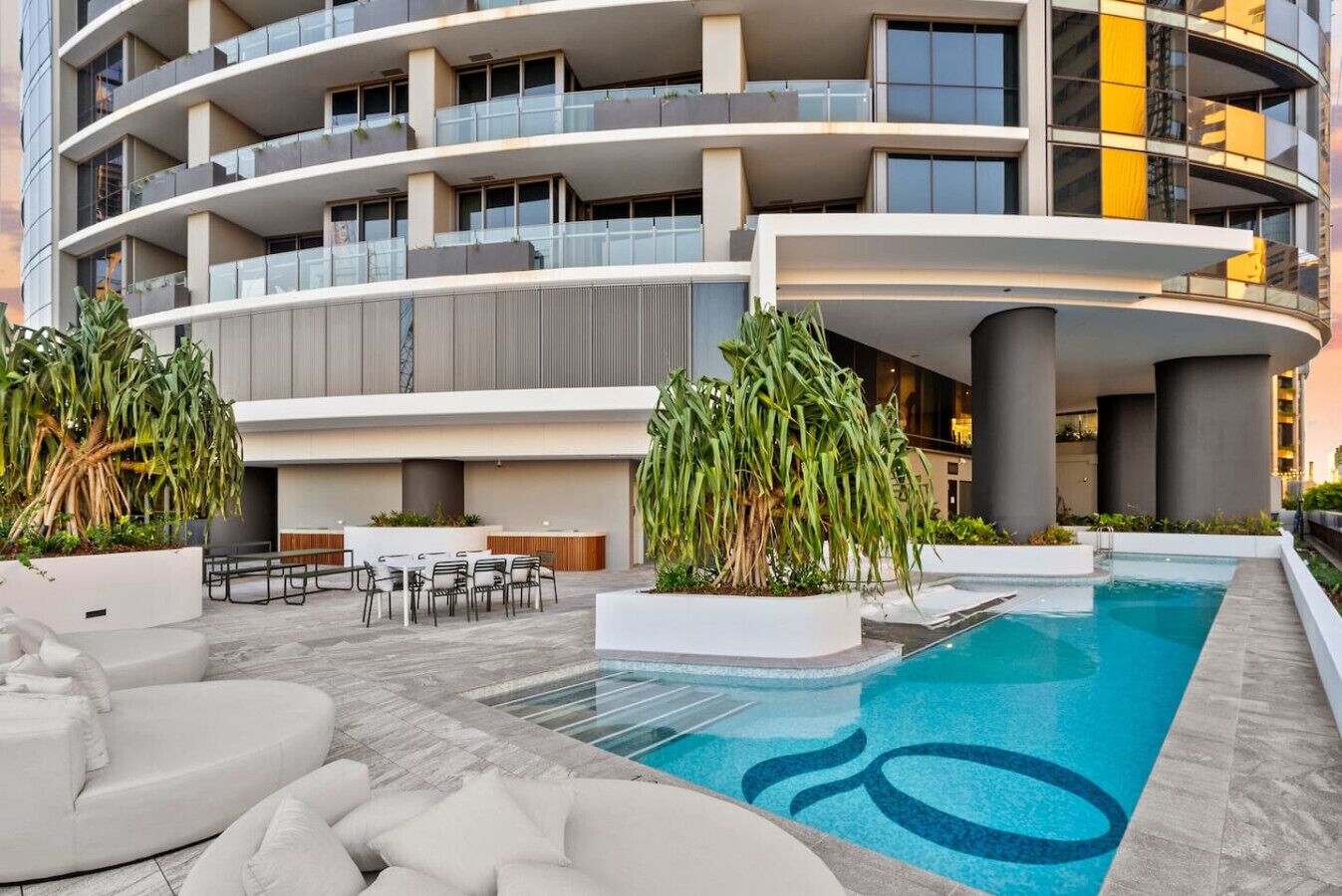 Un edificio moderno con piscina, zona de estar al aire libre y grandes macetas.