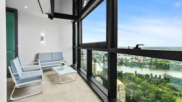 A modern room with a large window, a sofa, a coffee table, and a view of a river and cityscape.