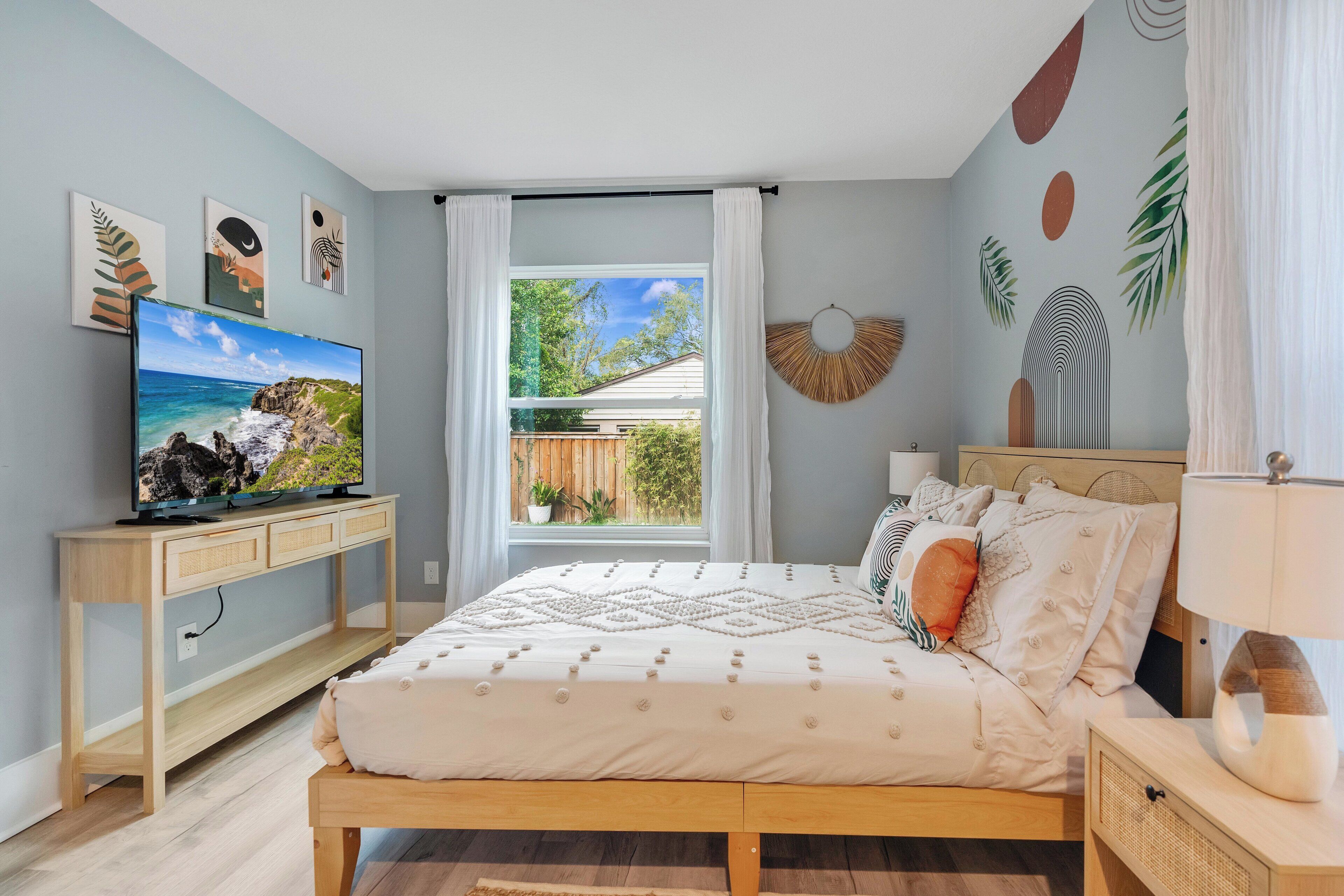 Een slaapkamer met een bed, een televisie op een standaard, een raam met gordijnen en wanddecoratie.